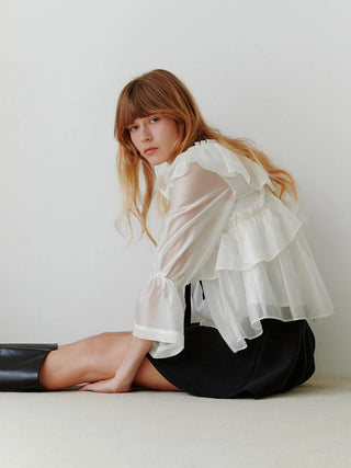 Side and back view of the SNIDEL ivory ribbon frill tunic on a seated model, showing layered ruffles and sheer sleeves.