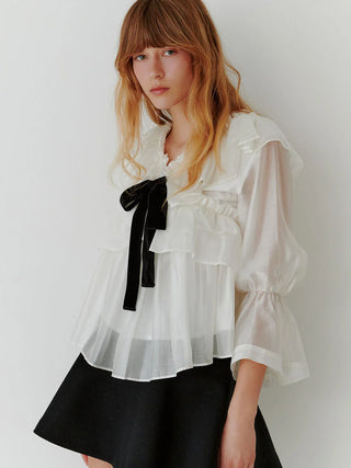 Model wearing the SNIDEL ivory ribbon frill tunic with sheer sleeves and a black velvet bow, paired with a black skirt.