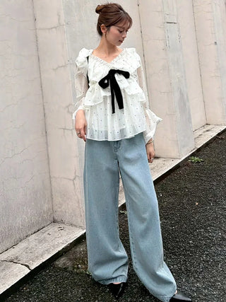 Model wearing a white dotted ribbon frill tunic with a black bow and wide-leg jeans outdoors.