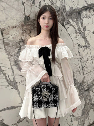 Model wearing the SNIDEL ivory ribbon frill tunic off the shoulders with matching shorts and a tweed handbag.