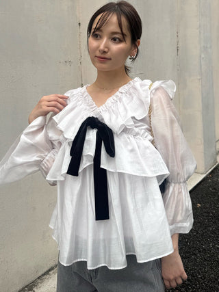 Model wearing the SNIDEL ivory ribbon frill tunic with jeans, showing the ruffled V-neckline and black velvet bow.