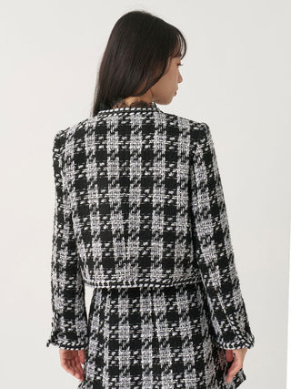 A woman shown from the back wearing a black and white tweed houndstooth jacket with matching skirt, against a plain white studio background.