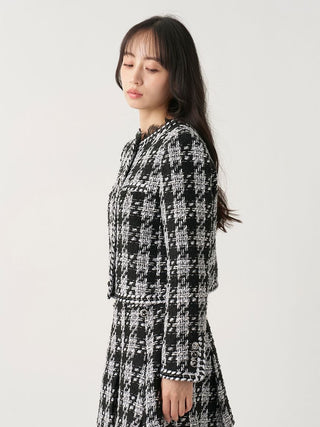 A woman wearing a black and white tweed jacket and matching skirt, photographed in profile against a plain light gray studio background.