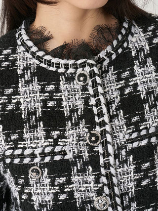 Close-up of a black and white tweed jacket with decorative buttons and a lace neckline, worn by a model.