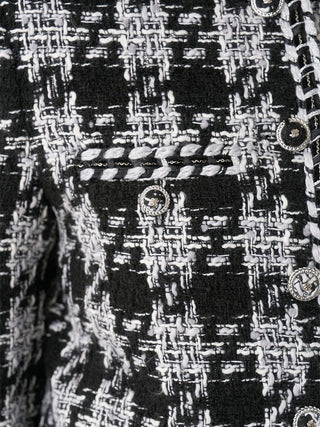 Close-up of a black and white tweed fabric with a woven houndstooth pattern, decorative braided trim, and ornate round buttons.