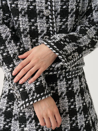 Close-up of a person wearing a black and white tweed jacket with a textured woven pattern, featuring a buttoned front and matching cuffs.