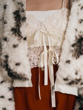 Close-up of the patterned SNIDEL Faux Fur Blouson's open zipper and ribbed hem over a white ribbon-tie lace top.