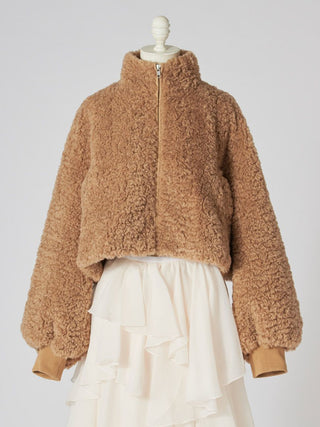 A cropped teddy fleece jacket in a warm camel brown color, styled on a mannequin with a cream ruffled skirt against a light gray background.