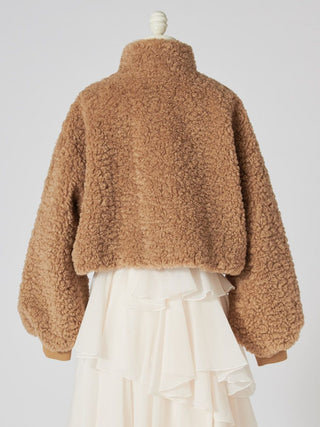 A cropped teddy fleece jacket in a warm camel brown color, shown from the back on a mannequin styled with a cream ruffled skirt against a light gray background.