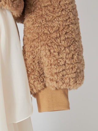 Close-up of a camel brown curly sherpa fleece jacket with a ribbed knit cuff, layered over a cream-colored satin dress.