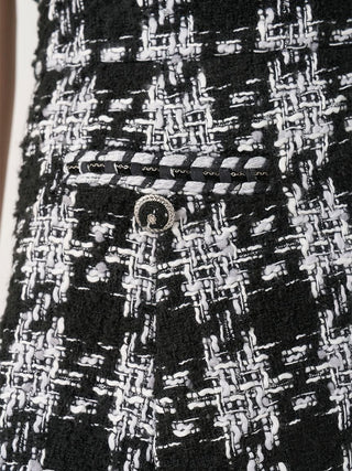 Close-up of a black and white tweed fabric with a woven houndstooth-like pattern, a black band with repeating white text, and a silver-toned circular embellishment.