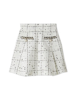 A white textured tweed mini skirt with a black grid pattern, featuring decorative cutout details on the front pockets and small black dot embellishments.