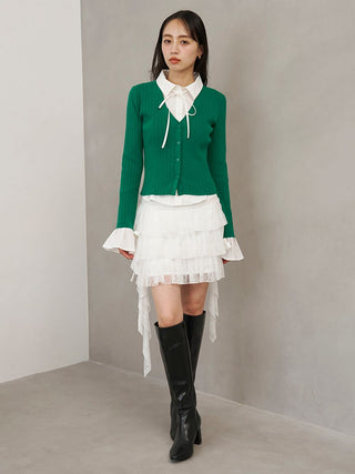 White SNIDEL Twist Frill Mini Skort styled with a green cardigan, white bow blouse and black knee-high boots.