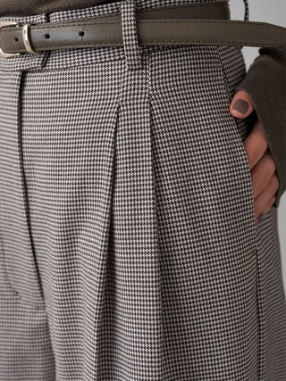 Close-up of the checked SNIDEL Belted Tuck Pants' front pleats and side pocket, with a hand tucked inside.