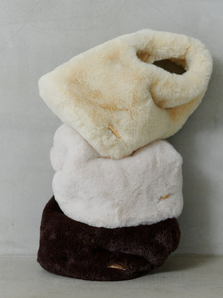 Three plush faux-fur slippers stacked vertically, with cream, off-white, and dark brown colors, set against a neutral gray background.