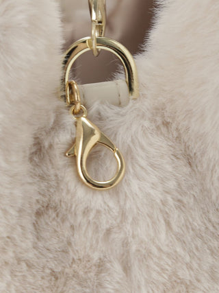 Close-up of a gold-tone lobster clasp and D-ring hardware attached to a soft, fluffy cream faux-fur or faux-leather material.