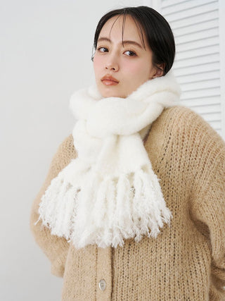 A woman wearing a thick, fluffy white scarf with fringe details and a beige knit cardigan, photographed against a clean white background.