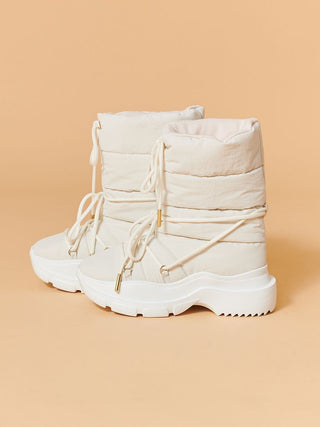 A pair of chunky off-white winter boots with thick platform soles and laces, shown against a solid peach background.