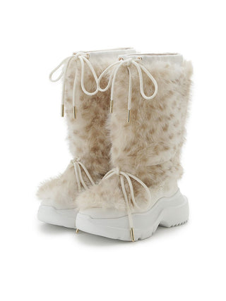 A pair of tall, fluffy faux-fur winter boots in a light beige and white pattern, featuring white laces with gold tips and chunky white platform soles with gold metal accents.