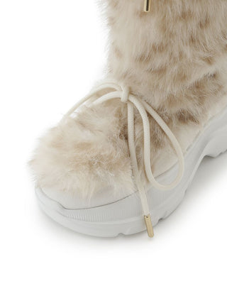 A close-up of a white and beige faux-fur winter boot with white laces and a chunky white sole, shown on a plain white background.