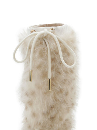 A close-up of a tall boot covered in fluffy cream faux fur, featuring a cream drawstring closure with gold-toned metal tips on a white background.