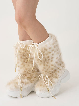 A pair of mid-calf furry boots with a beige and white leopard print pattern, featuring white laces with gold tips and chunky white platform soles, shown on a model's feet against a white studio background.