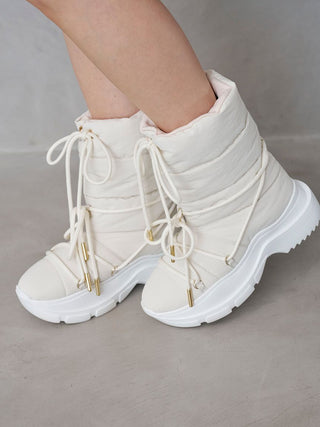 A pair of off-white quilted lace-up ankle boots with chunky white platform soles and small gold metal accents, shown on a model against a gray concrete background.