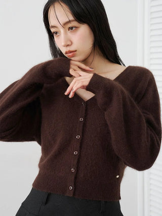 A woman wearing a dark brown fuzzy knit cardigan sweater with a V-neck and button closure, paired with black pants, set against a bright white background.
