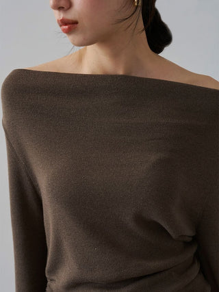 Close-up of a woman wearing a dark brown off-the-shoulder knit sweater against a light gray background.