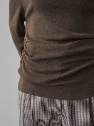Close-up of a brown ribbed knit top with ruching at the side, paired with a black-and-white houndstooth skirt against a light gray background.