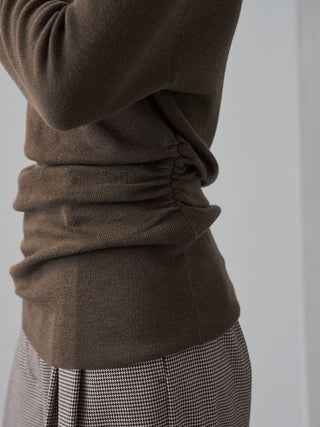 Close-up of a person wearing a dark brown ribbed knit top with ruching at the waist, paired with a black-and-white houndstooth skirt against a plain light gray background.