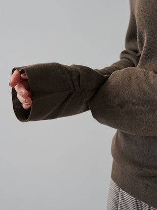 Close-up of a person wearing a ribbed knit sweater with wide, open cuffs, shown from the side against a plain light gray background.
