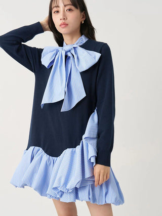 A model wearing a navy blue long-sleeve knit dress with light blue and white striped ruffle details at the collar in the shape of a bow and along the hem.