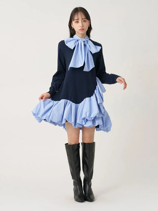 A model wearing a long-sleeve navy blue top with a light blue ruffled bow at the collar, paired with a matching light blue ruffled mini skirt and black knee-high boots, against a plain light gray studio background.
