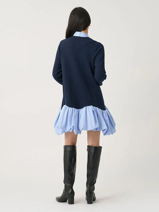 A model shown from the back wearing a navy blue long-sleeve top layered over a light blue and white striped ruffled mini skirt, paired with black knee-high boots, against a plain light gray studio background.