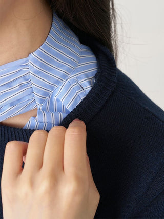 Close-up of a person wearing a navy blue knit sweater over a light blue and white striped shirt, with a hand adjusting the collar area.