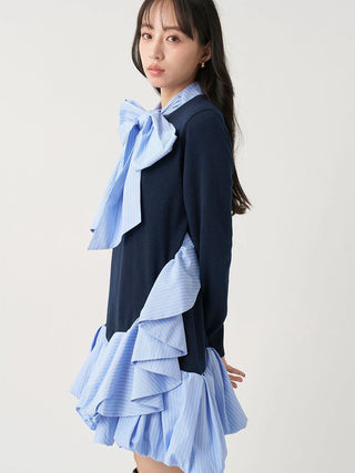 A model wearing a navy blue long-sleeve top with layered light blue and white striped ruffle details at the collar and hem, paired with a matching striped bow tie, against a plain light background.