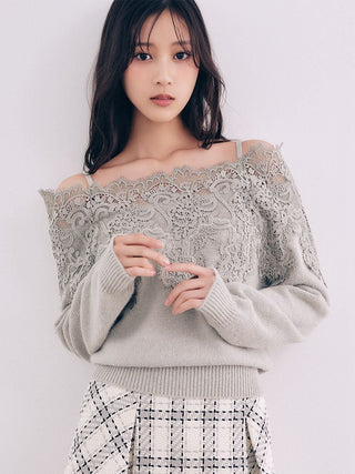 A woman wearing a light gray off-the-shoulder knit sweater with a large lace overlay and a black-and-white plaid skirt, photographed against a plain light background.