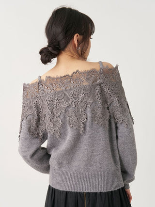 A woman shown from the back wearing a gray knit sweater with a wide lace yoke across the shoulders and upper back, paired with a dark skirt, against a plain light background.