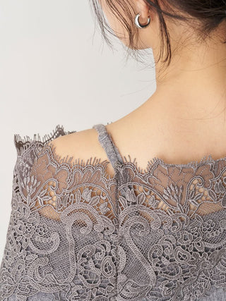 Close-up of a woman wearing a gray lace top with floral embroidery and thin straps, shown from the back against a light neutral background.
