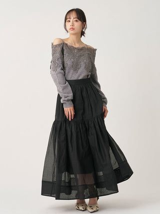 A model wearing a long-sleeve gray lace top and a black tiered tulle skirt, standing against a plain light gray studio background.