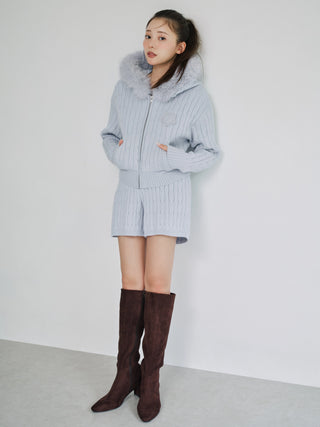 A woman models a light blue ribbed knit matching set consisting of a hooded jacket with a faux-fur collar and matching shorts, paired with dark brown suede over-the-knee boots, against a plain white wall.