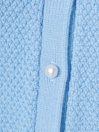 Close-up of a light blue textured knit cardigan or sweater with a single white pearl button on the front placket.