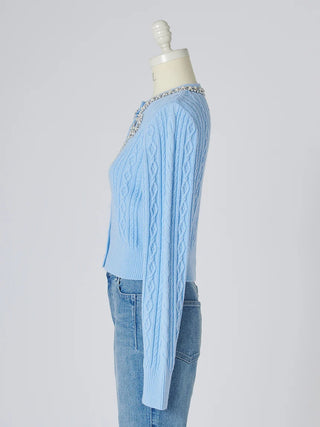 A light blue cable-knit cardigan sweater with a beaded neckline, displayed on a cream dress form mannequin paired with light-wash blue jeans against a light gray background.