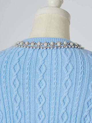A light blue cable-knit sweater displayed on a cream dress form, featuring a decorative collar embellished with white pearls and silver beads.