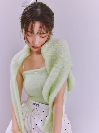 A woman wearing a light mint green fuzzy knit cardigan over a matching green camisole and white polka-dot skirt, posed against a soft lavender studio background.