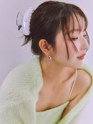 A woman with dark brown hair styled in a low bun with a white claw clip, wearing a light green knit cardigan and a matching green camisole. She is looking to the side, and a small silver earring is visible.