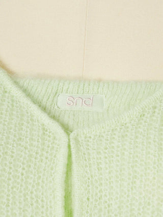 Close-up of a pale mint green knit cardigan with a visible 'snd' brand label at the neckline, set against a soft beige background.