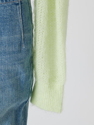 Close-up of a light lime green knit sweater sleeve with a ribbed cuff, shown next to blue denim jeans against a plain light gray background.