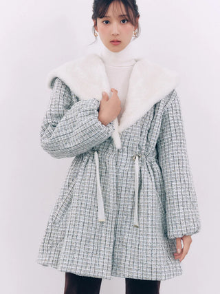 A model wearing a light gray and white tweed coat with a large white faux-fur collar, styled over a white turtleneck sweater.